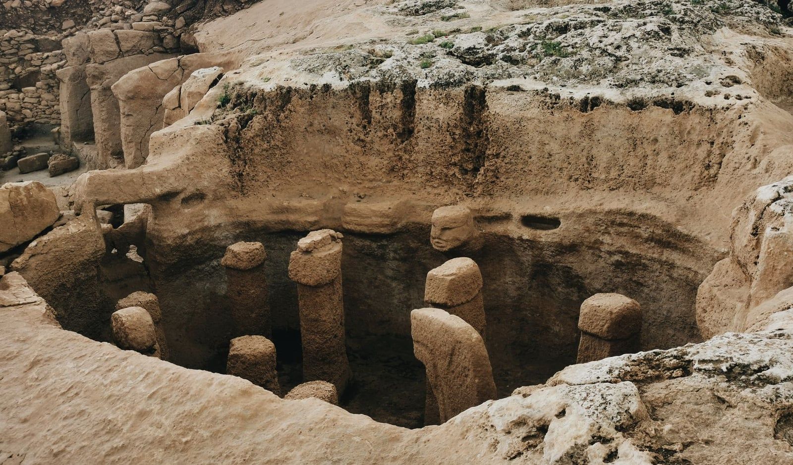 Rock-cut chamber featuring upright stone pillars and a carved human head at Karahan Tepe, a prehistoric sister site of Göbekli Tepe in Turkey.