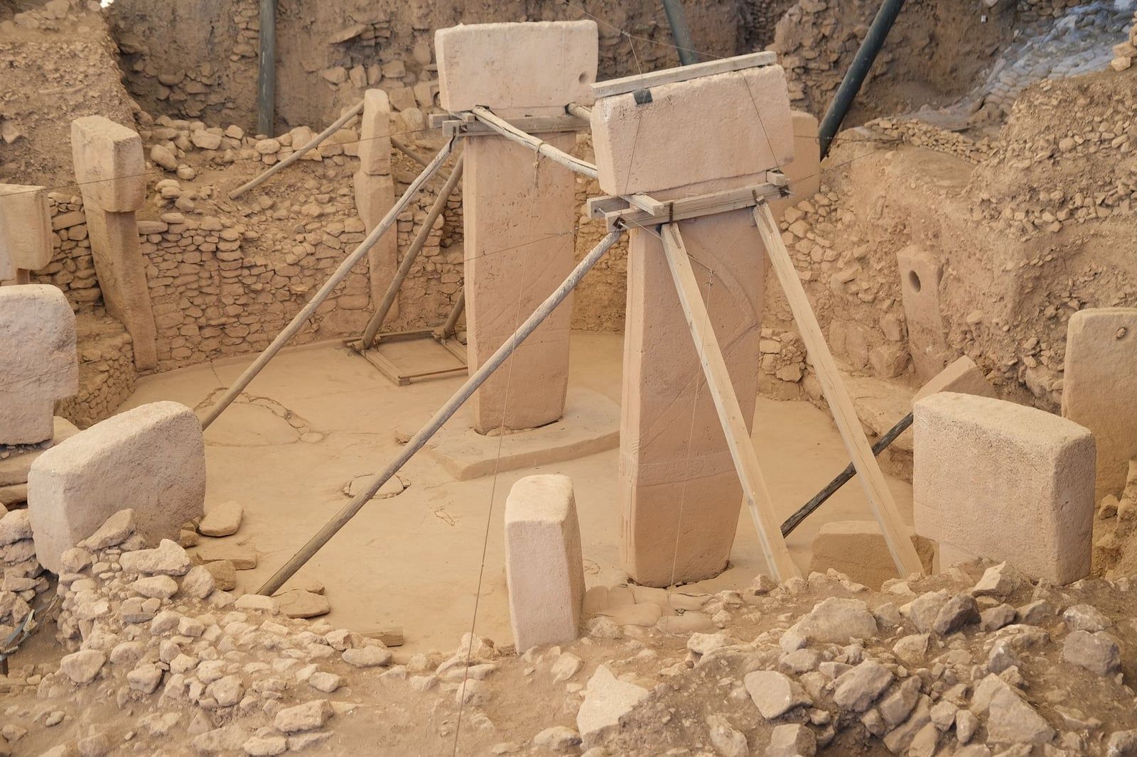 Ancient T-shaped stone pillars reinforced with support braces stand within a circular excavated enclosure at Göbekli Tepe.