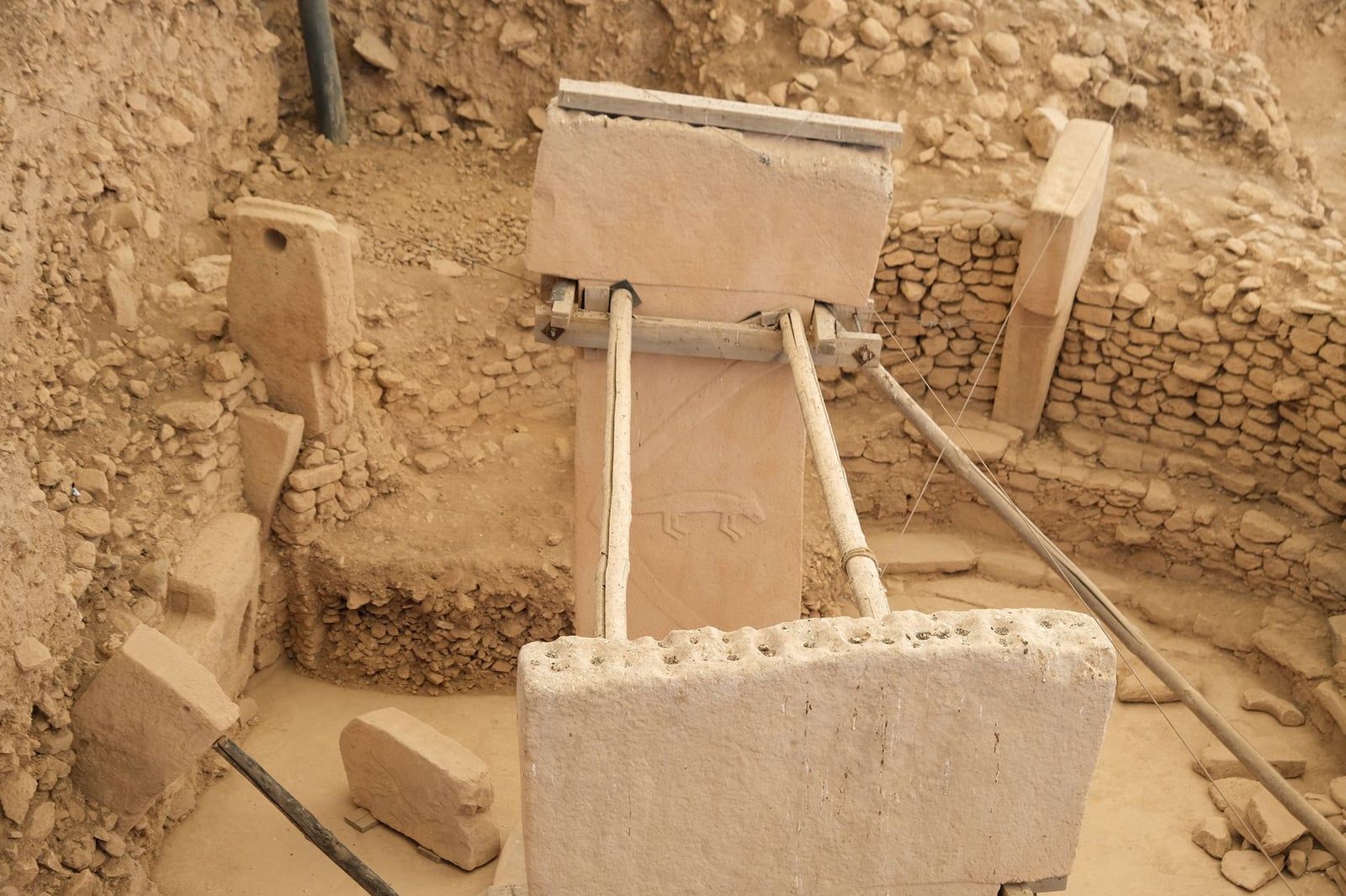 A low-relief animal carving on a limestone T-shaped pillar supported by conservation struts at Göbekli Tepe.